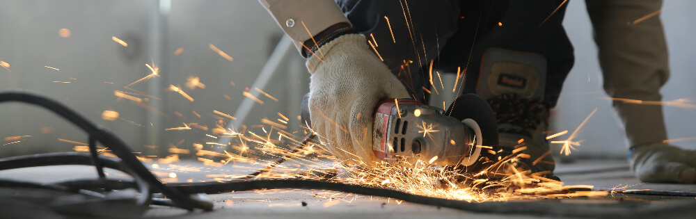 Eine Person arbeitet mit einem Winkelschleifer und erzeugt Funken. Sie trägt Arbeitshandschuhe und bearbeitet eine Metalloberfläche, während Funken sprühen.